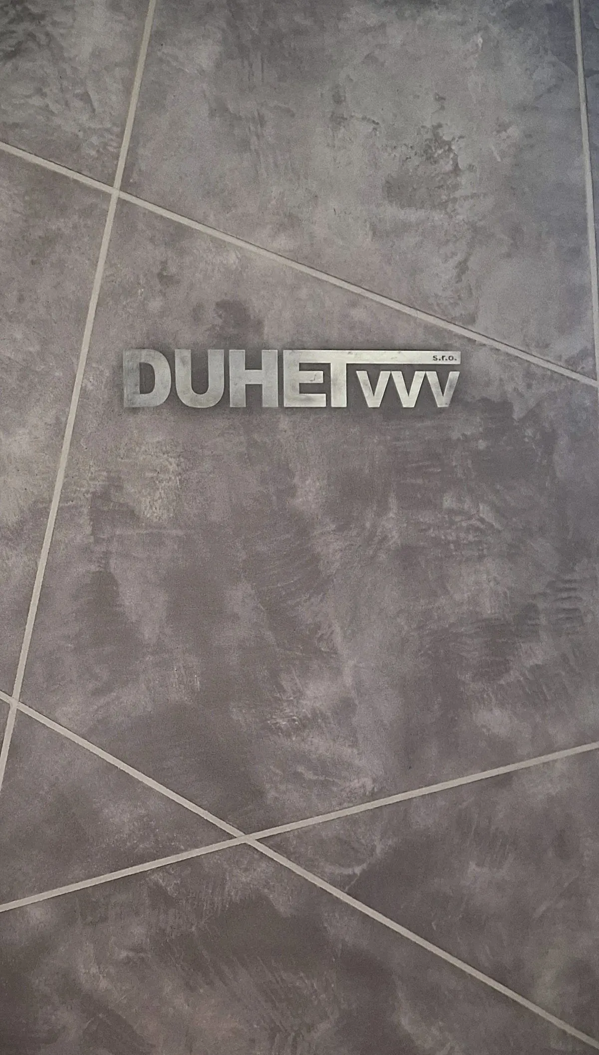 Designová stěna s betonovou stěrkou a kovovým logem DUHET vvv