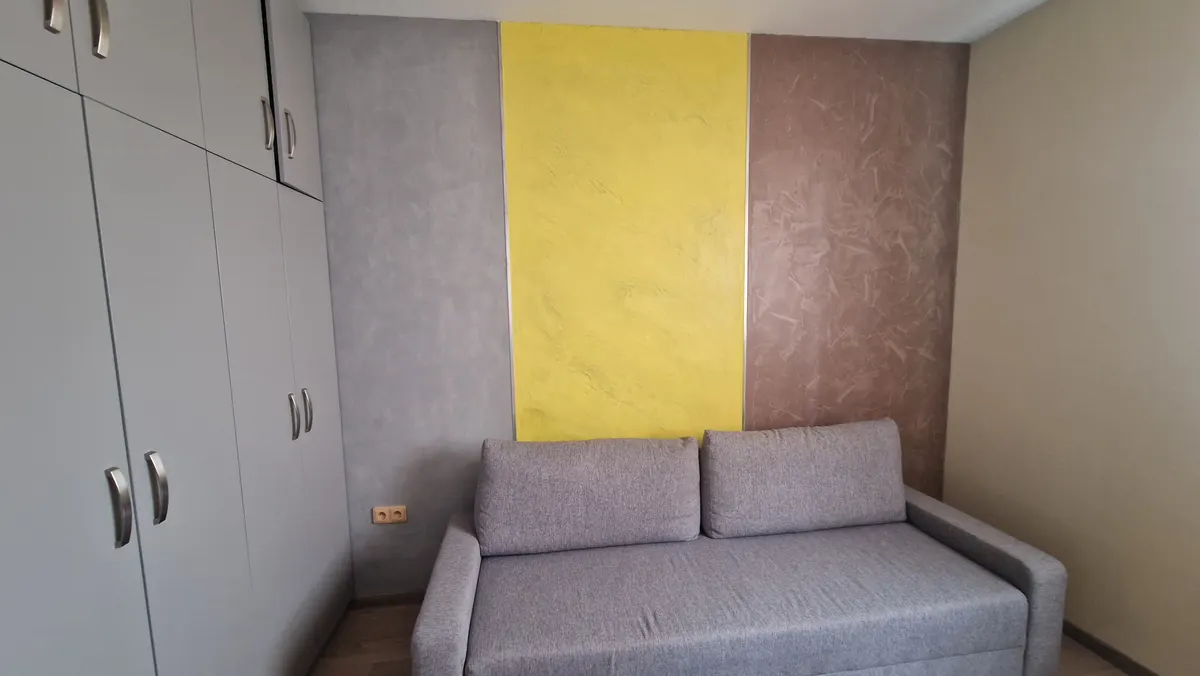 Pokoj s pohovkou před stěnou ze tří pásů stěrky v šedé, žluté a hnědé barvě